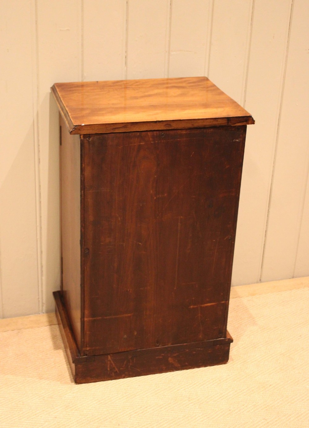 A late 19th-century walnut bedside cabinet featuring a single door with incised geometric detail, a brass drop handle, and a solid plinth base. View XI