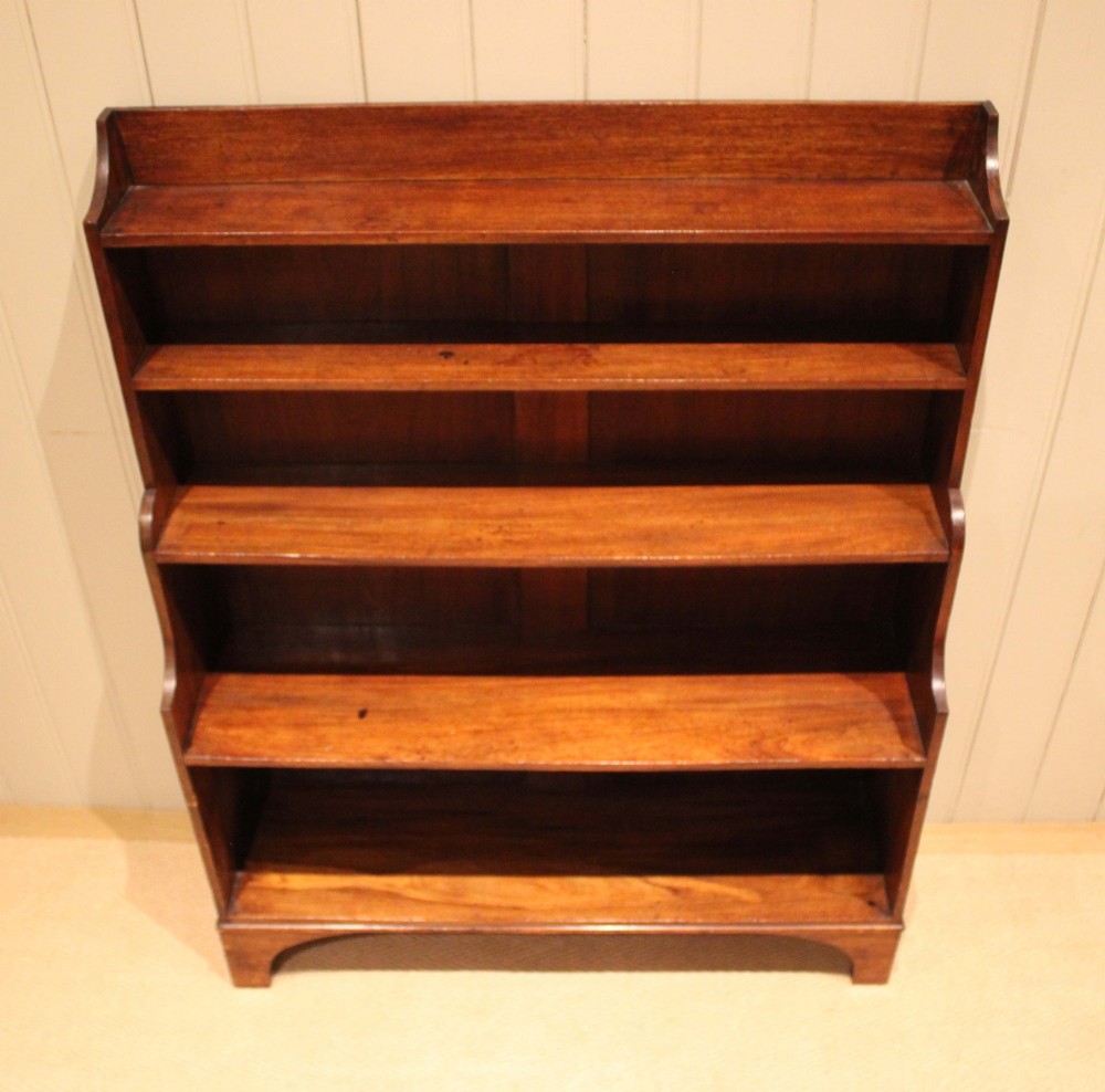 An antique Regency mahogany open bookcase featuring four fixed shelves, graduated side panels, and a shaped apron base. View VI