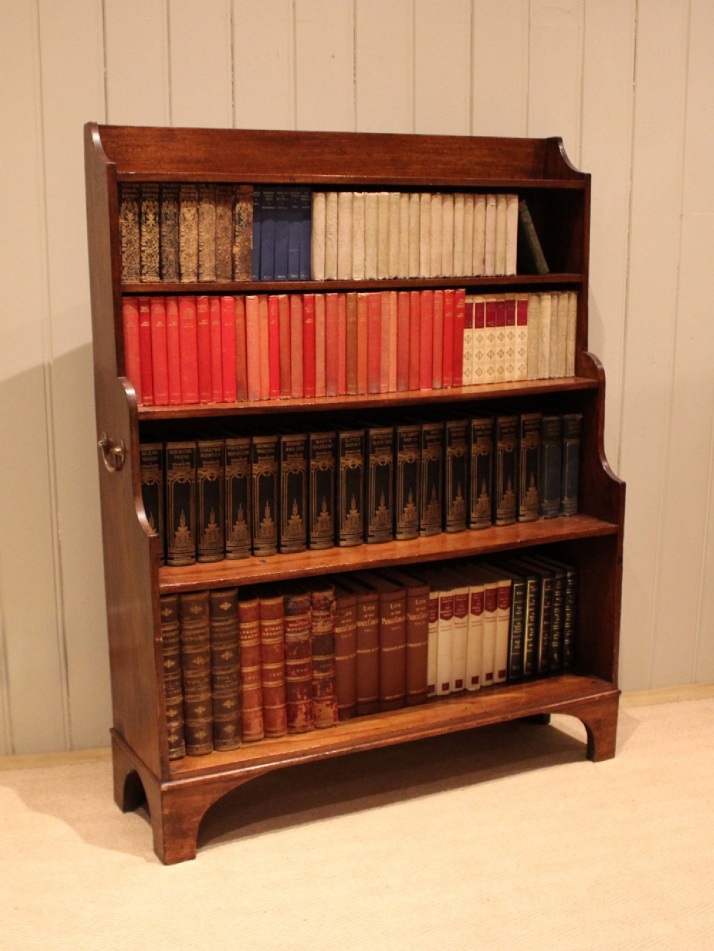 An antique Regency mahogany open bookcase featuring four fixed shelves, graduated side panels, and a shaped apron base. View VII