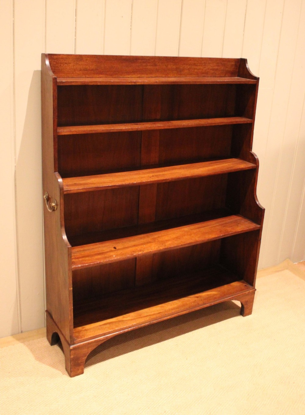 An antique Regency mahogany open bookcase featuring four fixed shelves, graduated side panels, and a shaped apron base. View VIII