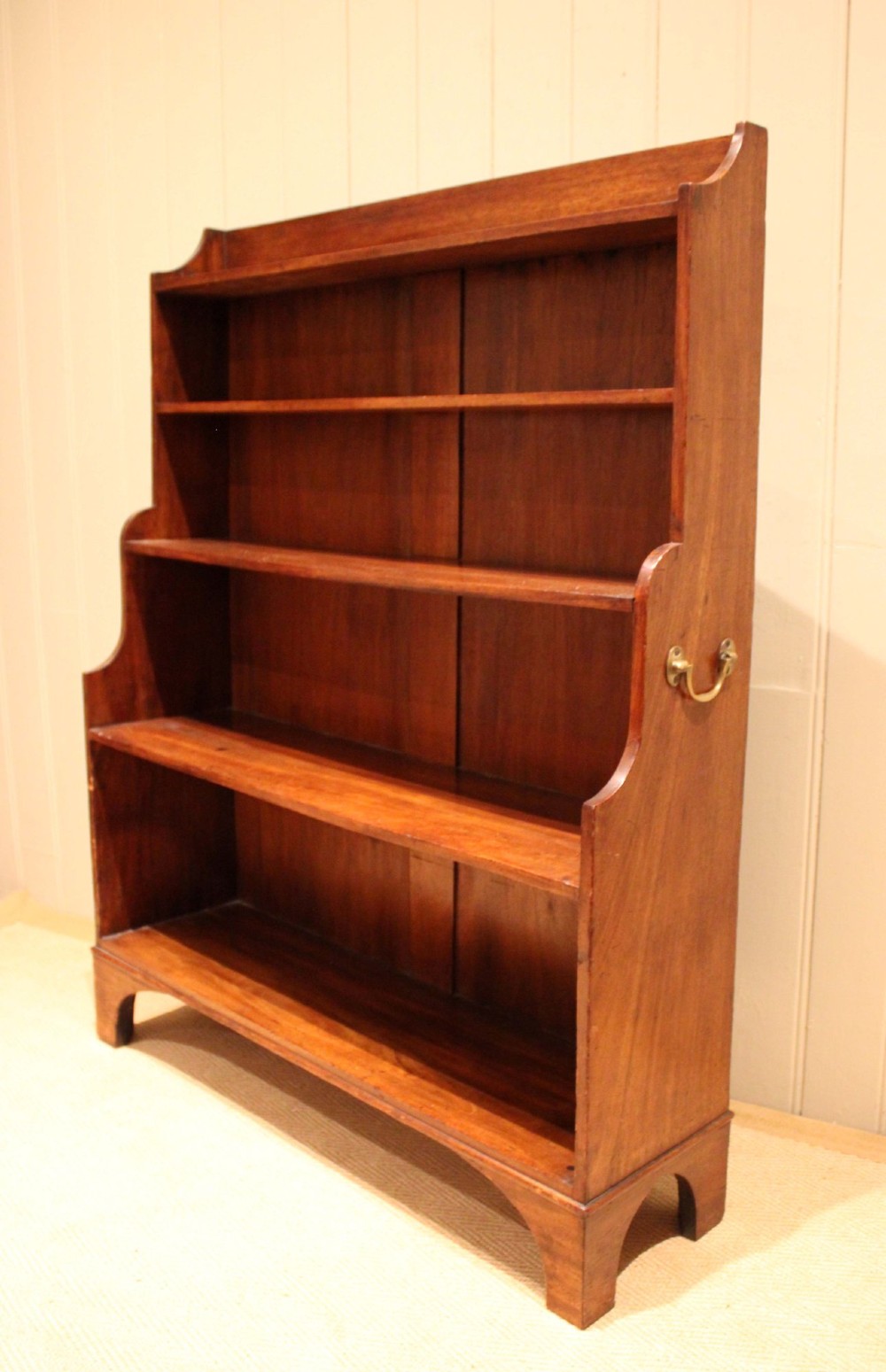 An antique Regency mahogany open bookcase featuring four fixed shelves, graduated side panels, and a shaped apron base. View X