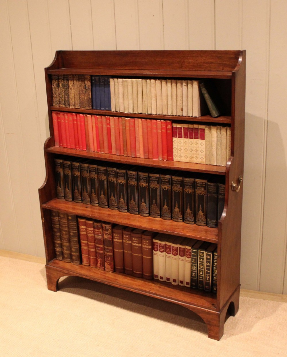 An antique Regency mahogany open bookcase featuring four fixed shelves, graduated side panels, and a shaped apron base. View XI