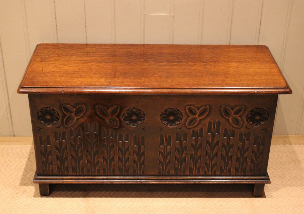 A rectangular solid oak coffer featuring stylized floral and botanical carvings across the front panel with a smooth hinged lid. View II