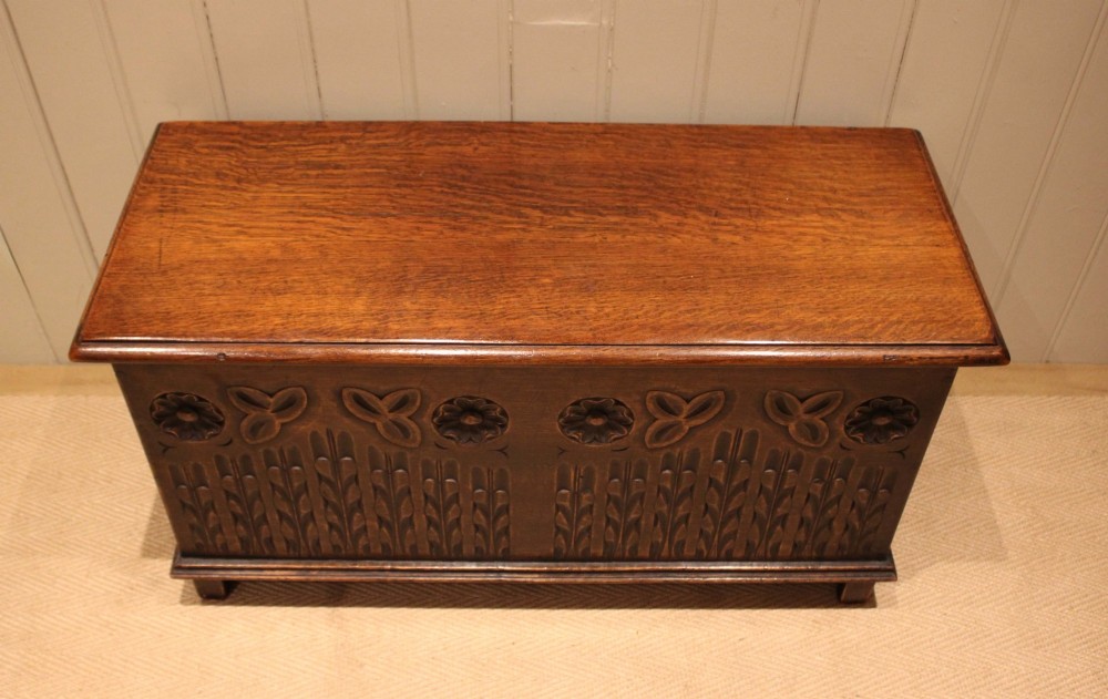 A rectangular solid oak coffer featuring stylized floral and botanical carvings across the front panel with a smooth hinged lid. View V