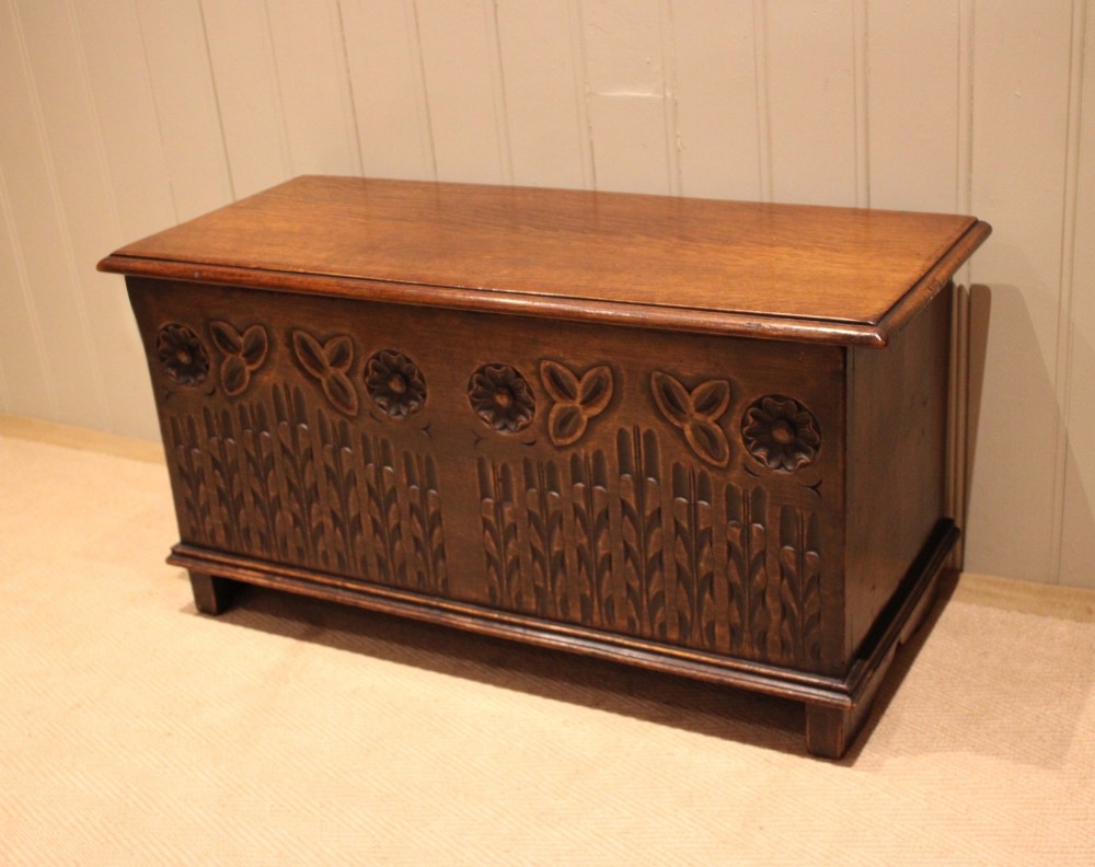 A rectangular solid oak coffer featuring stylized floral and botanical carvings across the front panel with a smooth hinged lid. View VI