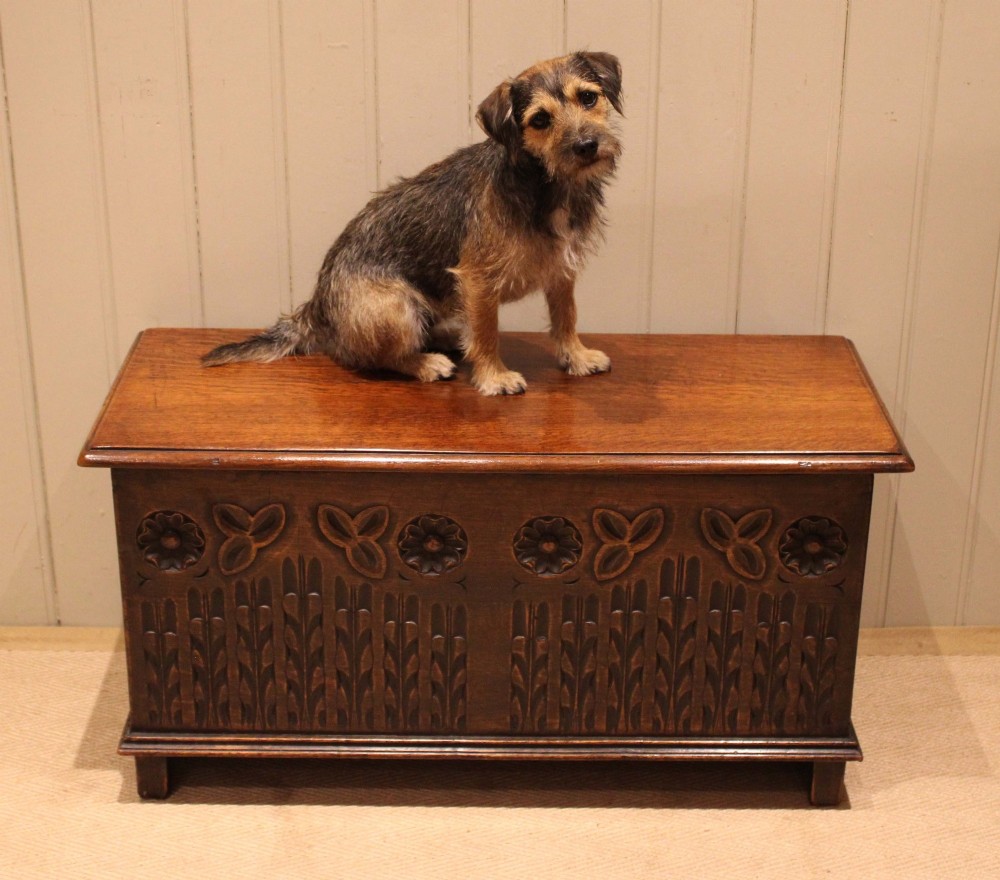 A rectangular solid oak coffer featuring stylized floral and botanical carvings across the front panel with a smooth hinged lid. View VII