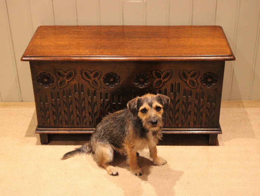 A rectangular solid oak coffer featuring stylized floral and botanical carvings across the front panel with a smooth hinged lid. View IX