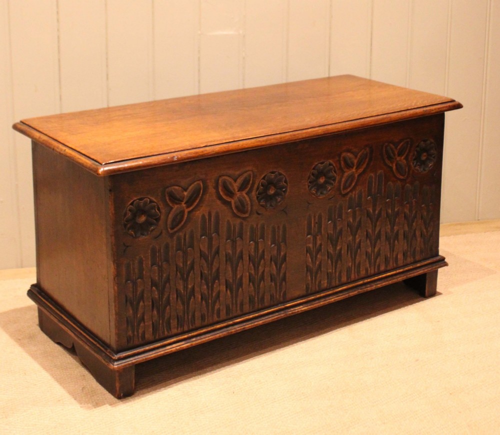 A rectangular solid oak coffer featuring stylized floral and botanical carvings across the front panel with a smooth hinged lid. View X