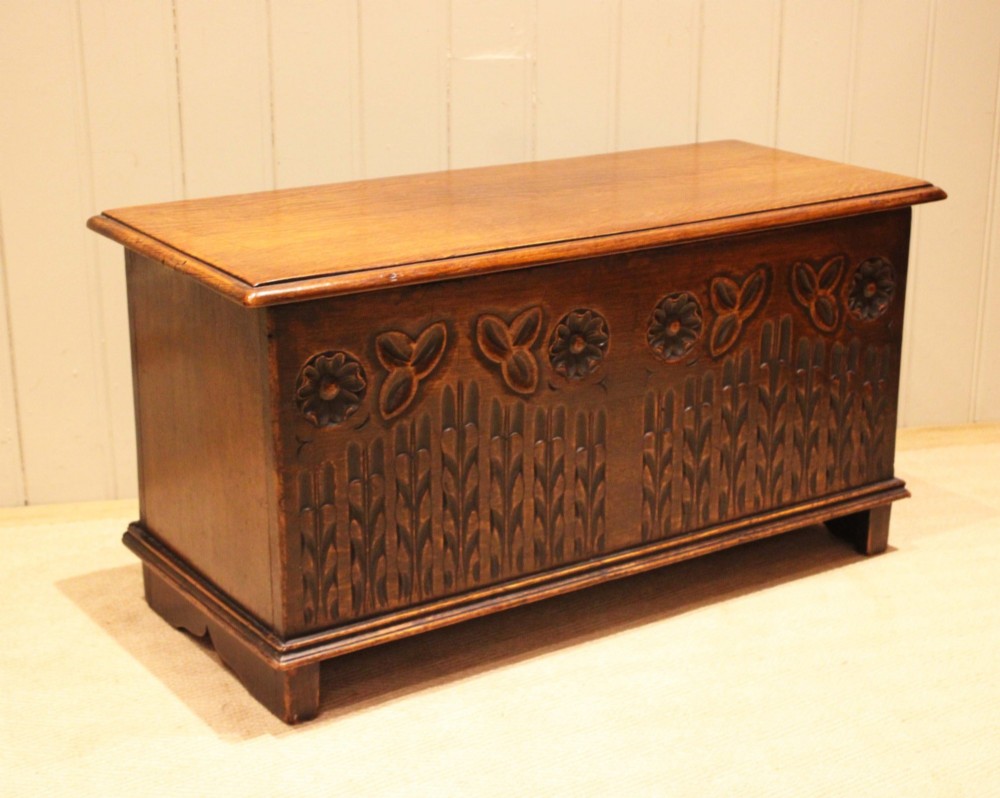 A rectangular solid oak coffer featuring stylized floral and botanical carvings across the front panel with a smooth hinged lid. View XI