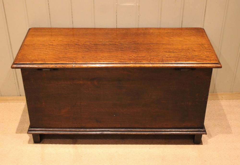 A rectangular solid oak coffer featuring stylized floral and botanical carvings across the front panel with a smooth hinged lid. View XII