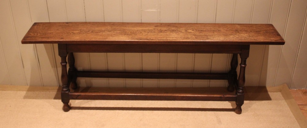 A long solid oak bench featuring a flat timber seat supported by four turned legs and a low rectangular stretcher base.