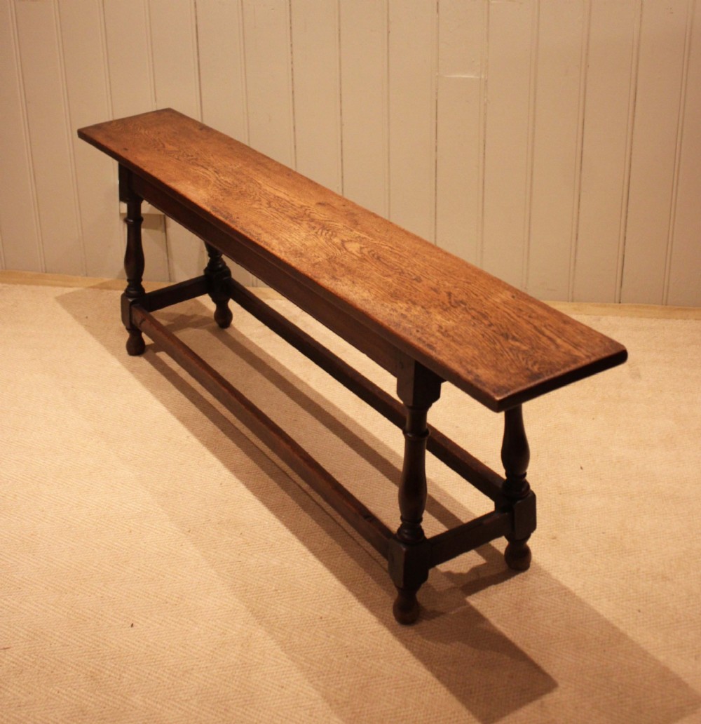 A long solid oak bench featuring a flat timber seat supported by four turned legs and a low rectangular stretcher base. View II