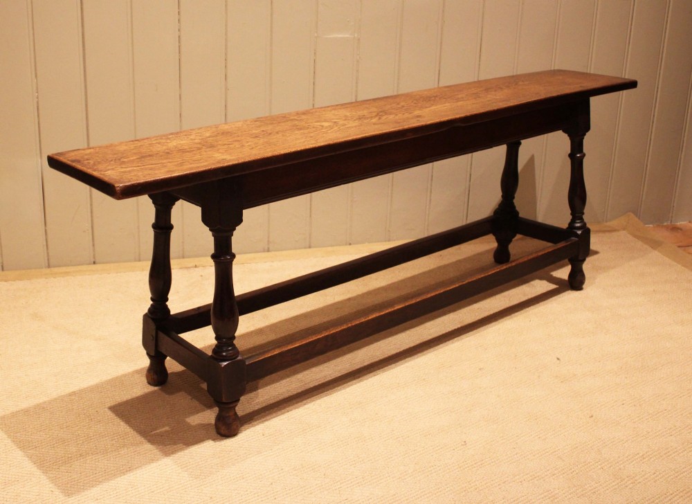 A long solid oak bench featuring a flat timber seat supported by four turned legs and a low rectangular stretcher base. View III