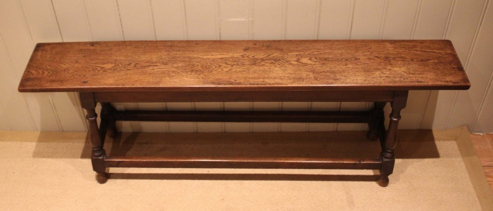 A long solid oak bench featuring a flat timber seat supported by four turned legs and a low rectangular stretcher base. View IV