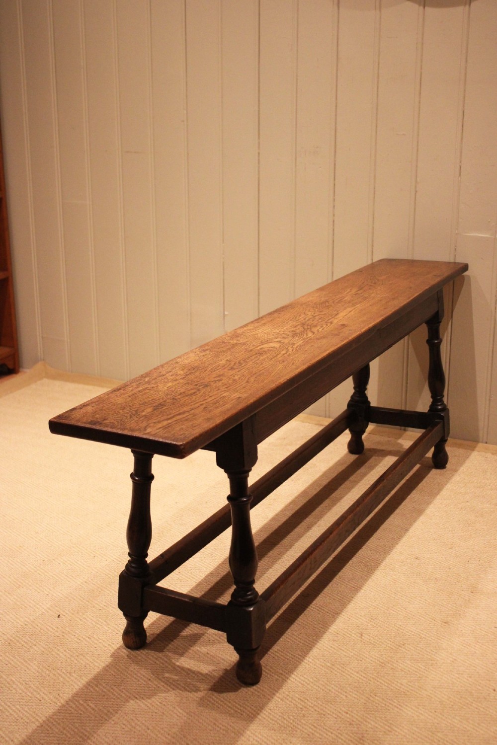 A long solid oak bench featuring a flat timber seat supported by four turned legs and a low rectangular stretcher base. View V