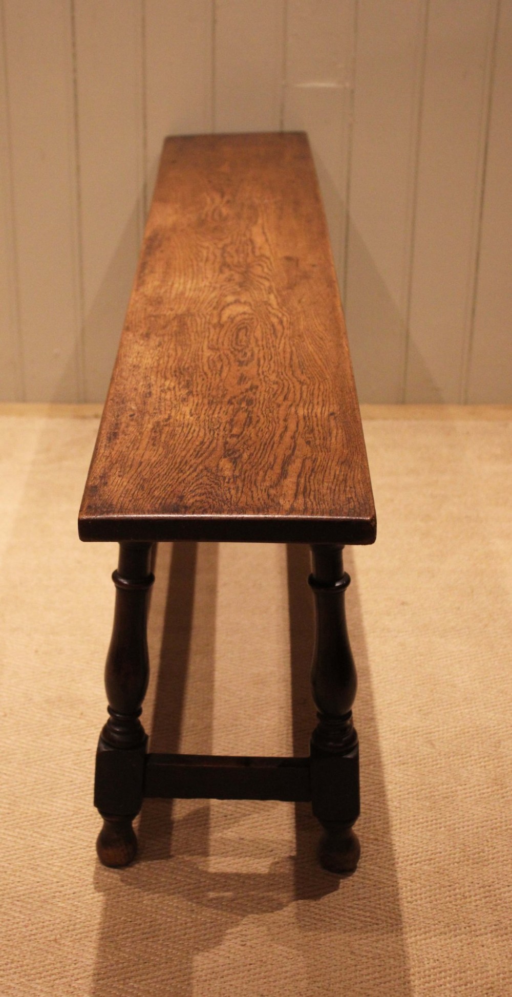 A long solid oak bench featuring a flat timber seat supported by four turned legs and a low rectangular stretcher base. View VI