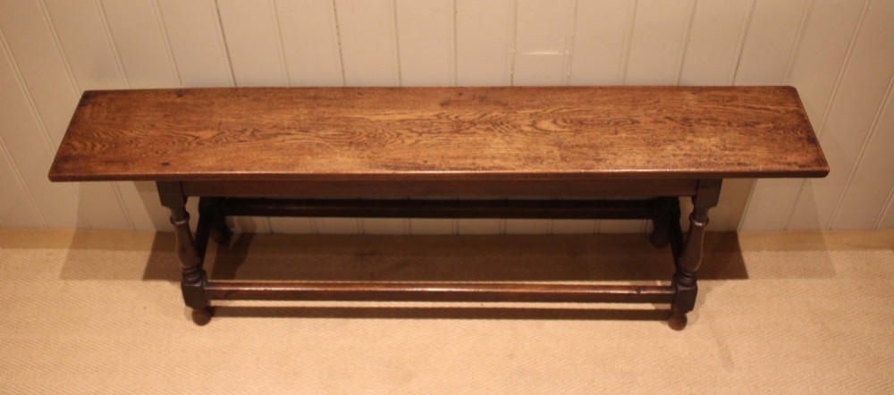 A long solid oak bench featuring a flat timber seat supported by four turned legs and a low rectangular stretcher base. View VII
