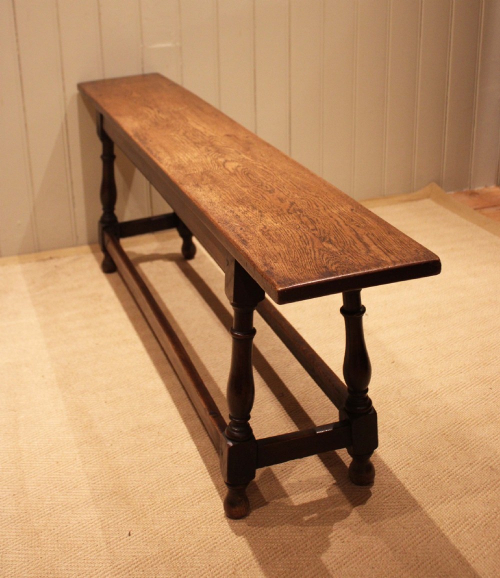 A long solid oak bench featuring a flat timber seat supported by four turned legs and a low rectangular stretcher base. View VIII