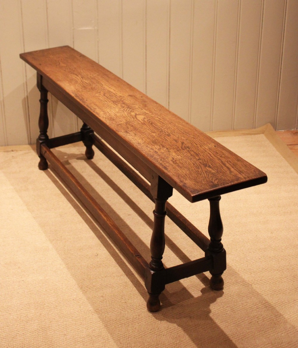 A long solid oak bench featuring a flat timber seat supported by four turned legs and a low rectangular stretcher base. View IX