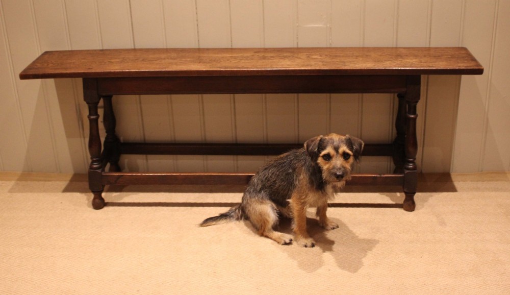 A long solid oak bench featuring a flat timber seat supported by four turned legs and a low rectangular stretcher base. View XII