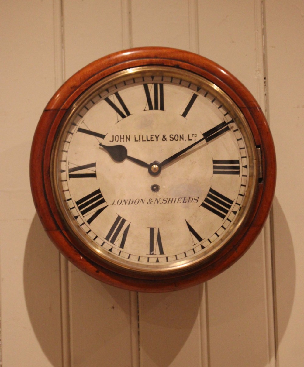 A circular late nineteenth-century Victorian wall clock featuring a turned mahogany frame, a polished brass bezel, and a cream dial with black Roman numerals. View II
