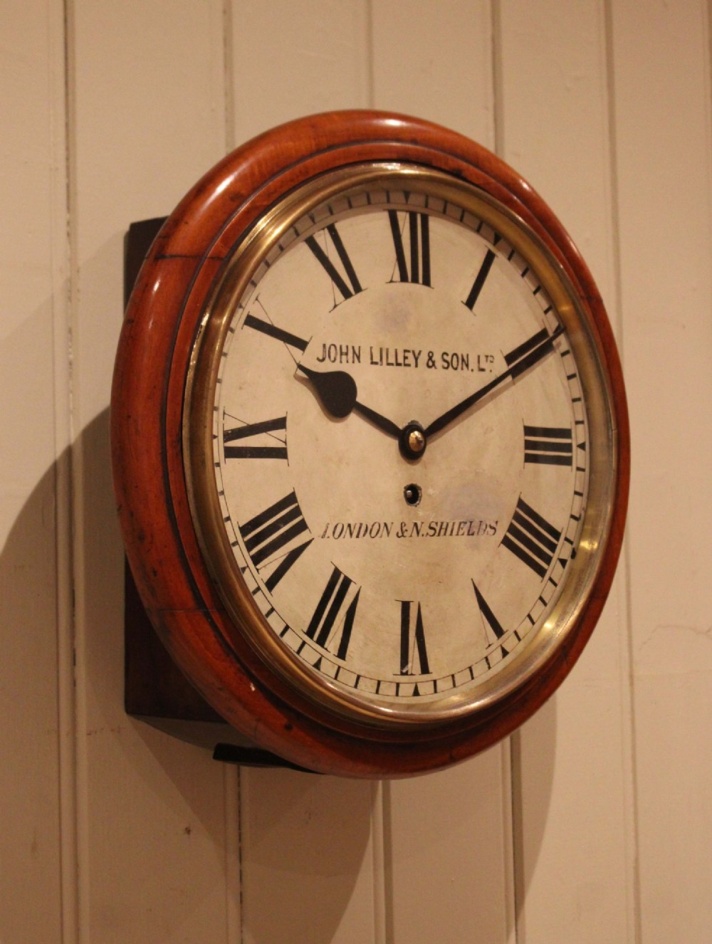 A circular late nineteenth-century Victorian wall clock featuring a turned mahogany frame, a polished brass bezel, and a cream dial with black Roman numerals. View VI