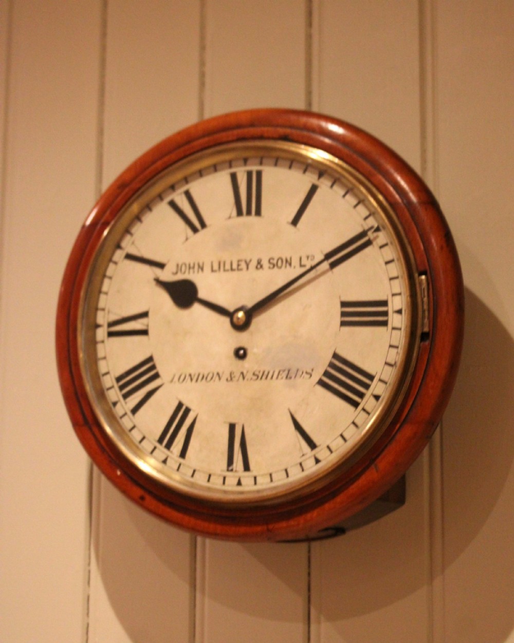 A circular late nineteenth-century Victorian wall clock featuring a turned mahogany frame, a polished brass bezel, and a cream dial with black Roman numerals. View VII