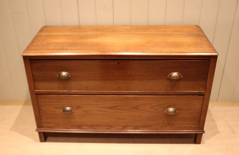 A wide low oak chest of drawers featuring two deep drawers with brass shell cup handles and panelled side construction. View II
