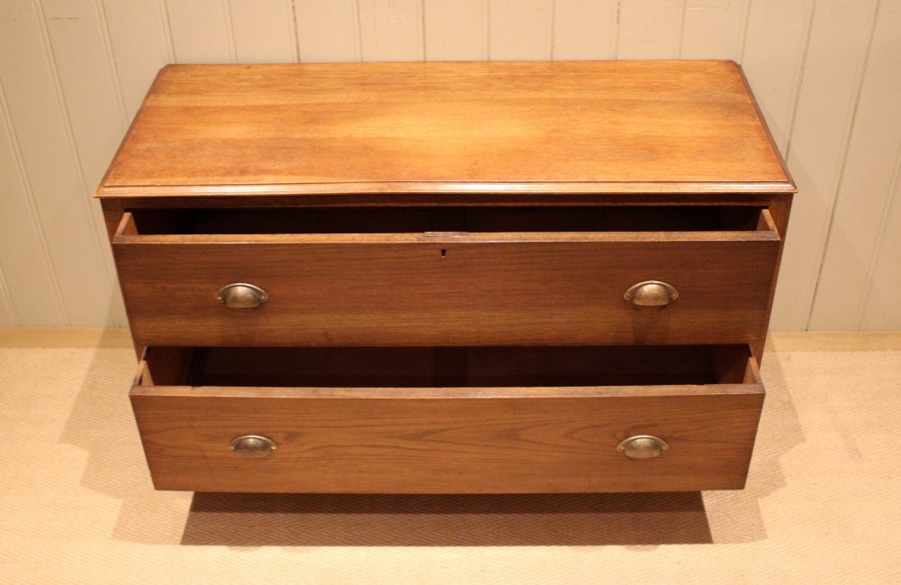 A wide low oak chest of drawers featuring two deep drawers with brass shell cup handles and panelled side construction. View V