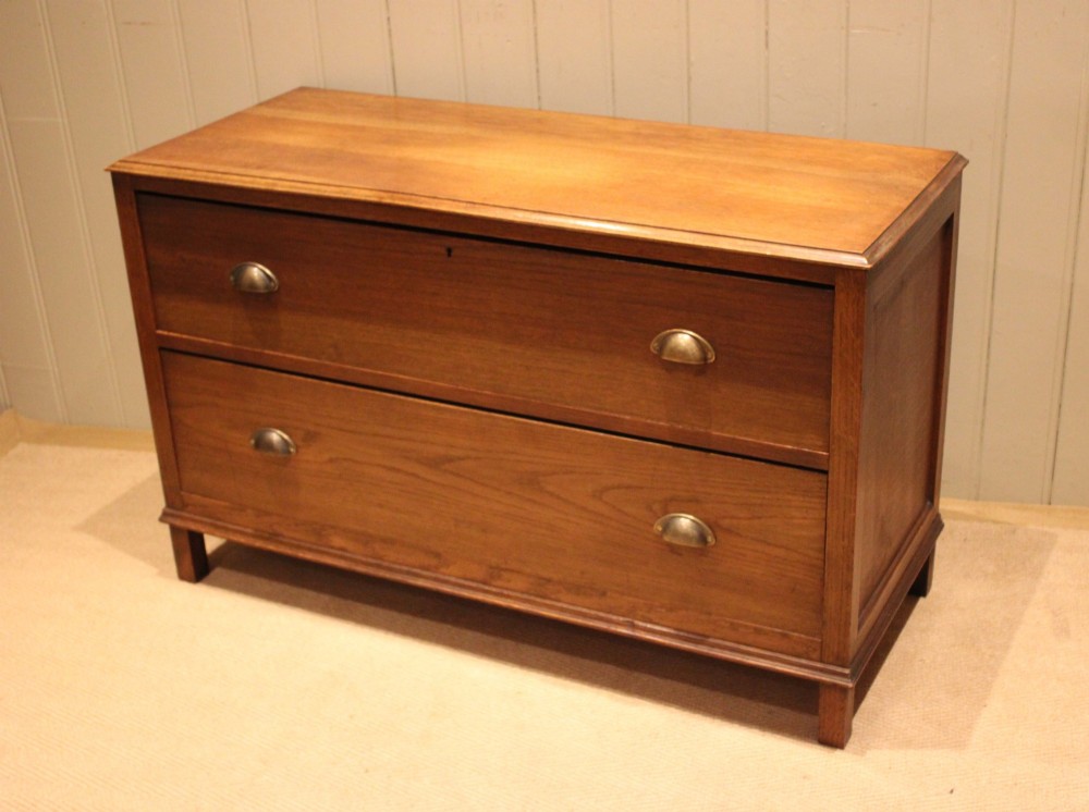 A wide low oak chest of drawers featuring two deep drawers with brass shell cup handles and panelled side construction. View VII