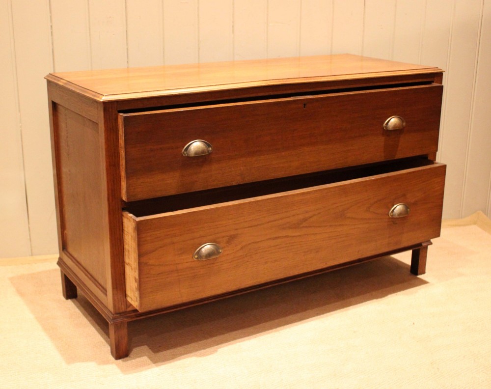 A wide low oak chest of drawers featuring two deep drawers with brass shell cup handles and panelled side construction. View VIII