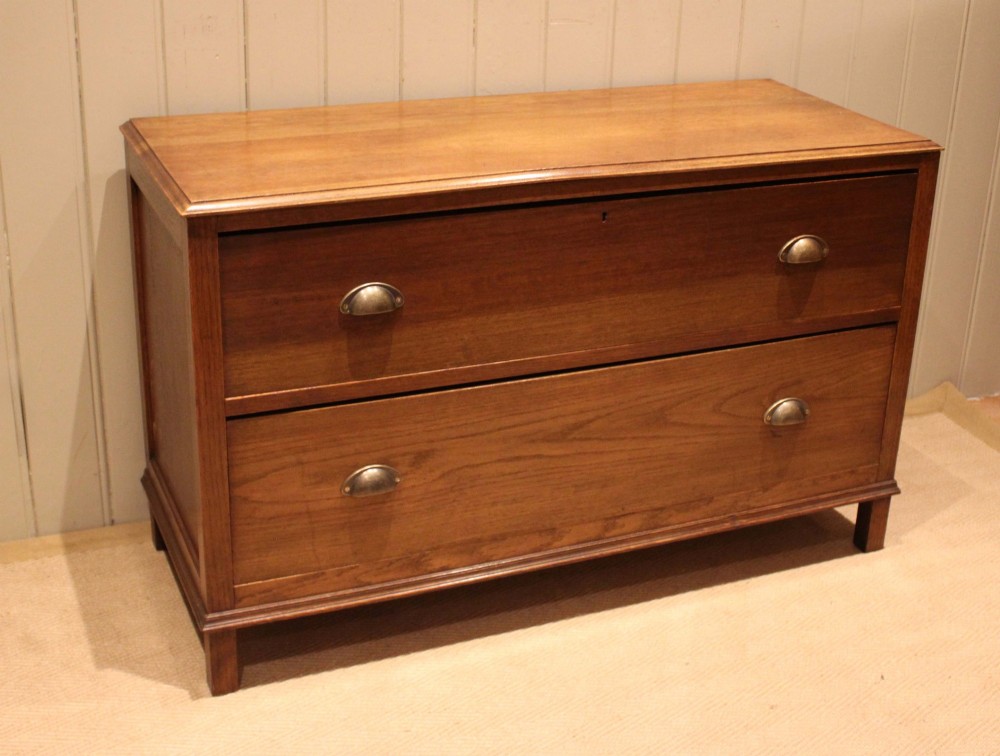 A wide low oak chest of drawers featuring two deep drawers with brass shell cup handles and panelled side construction. View IX
