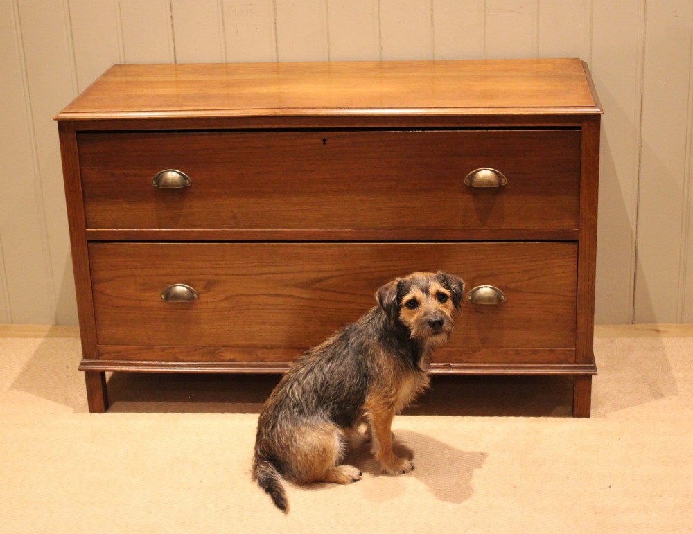 A wide low oak chest of drawers featuring two deep drawers with brass shell cup handles and panelled side construction. View X