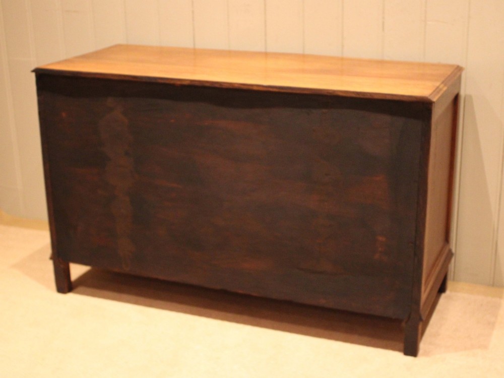 A wide low oak chest of drawers featuring two deep drawers with brass shell cup handles and panelled side construction. View XII