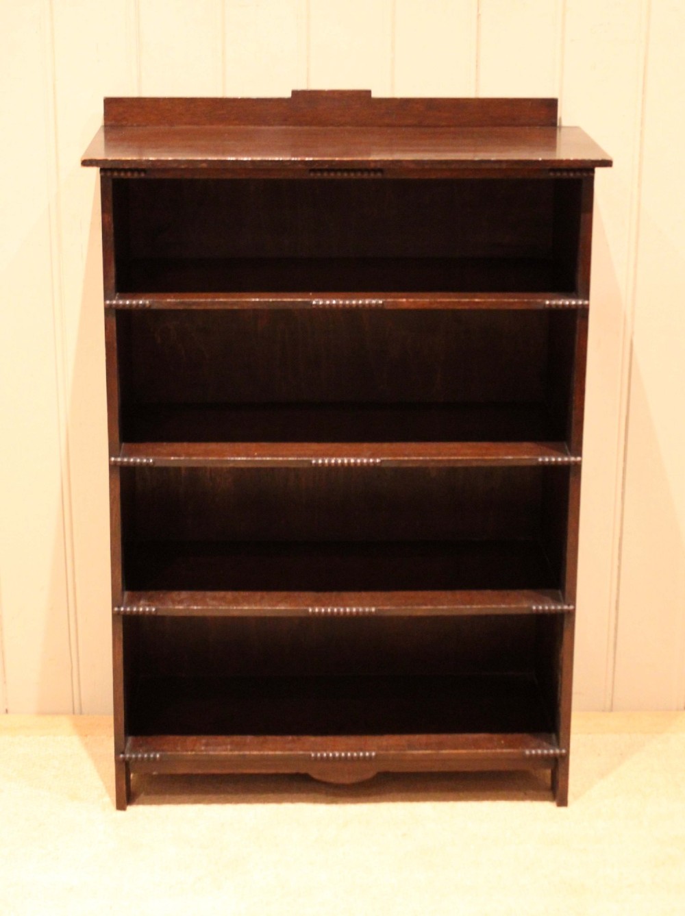 A dark oak open bookcase featuring four horizontal shelves with beaded front edges and a low raised gallery back. View II