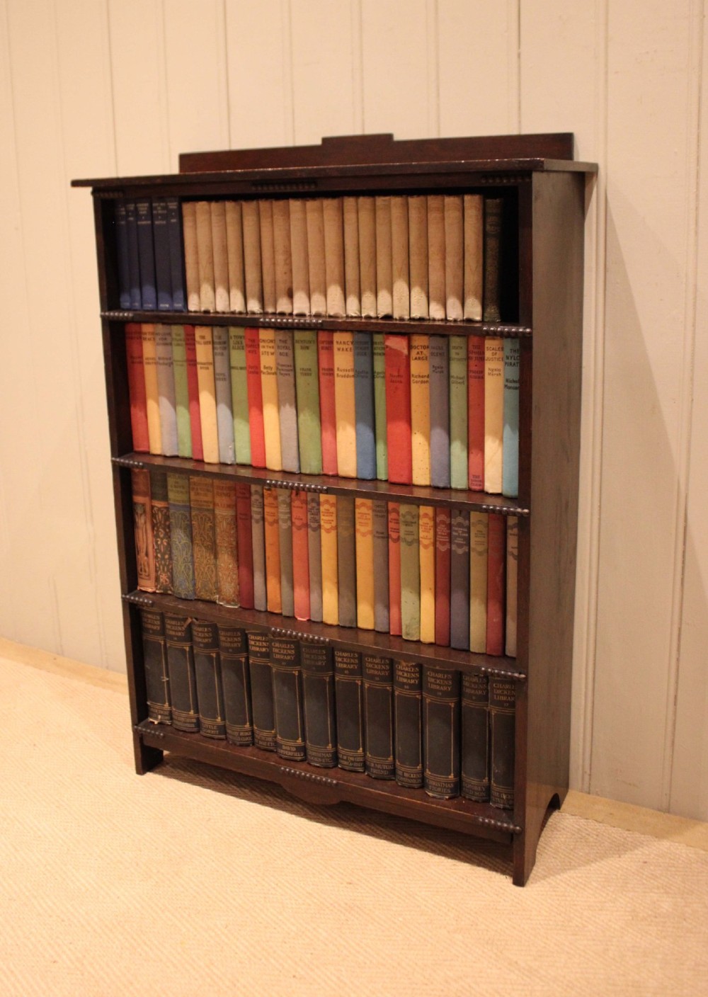 A dark oak open bookcase featuring four horizontal shelves with beaded front edges and a low raised gallery back. View V