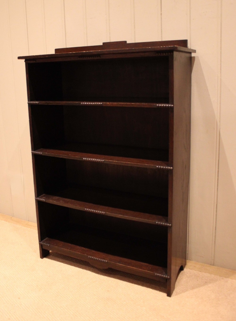 A dark oak open bookcase featuring four horizontal shelves with beaded front edges and a low raised gallery back. View VI