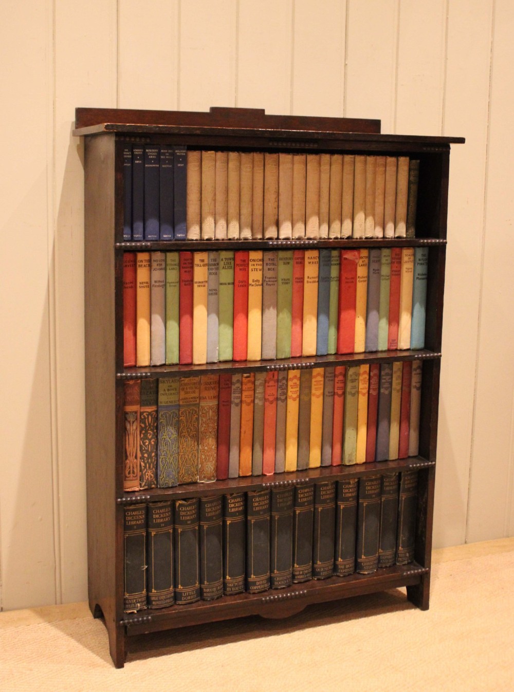 A dark oak open bookcase featuring four horizontal shelves with beaded front edges and a low raised gallery back. View VII