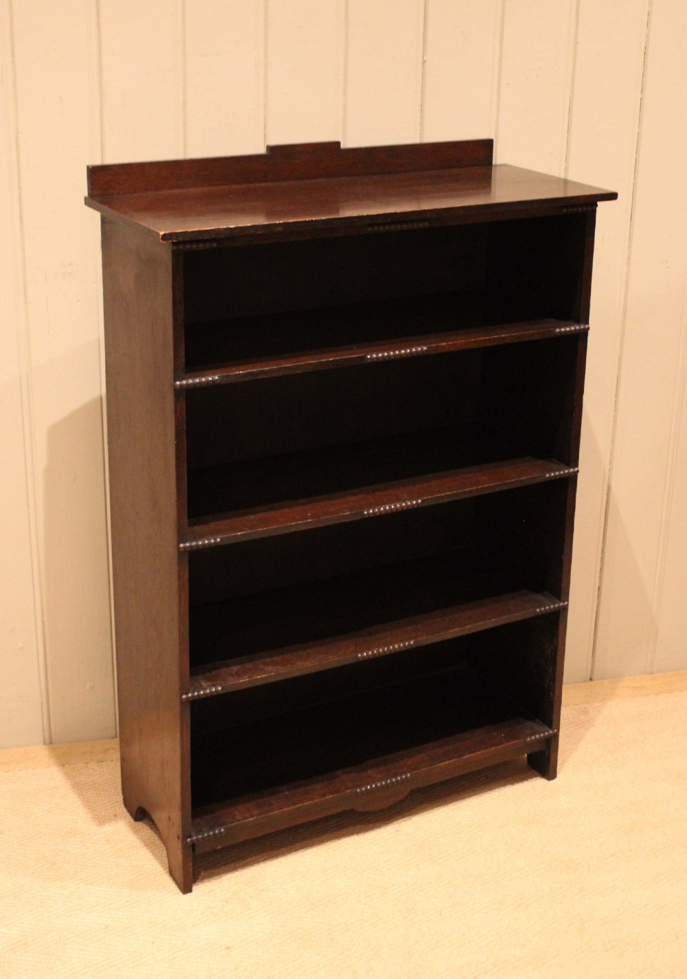 A dark oak open bookcase featuring four horizontal shelves with beaded front edges and a low raised gallery back. View VIII