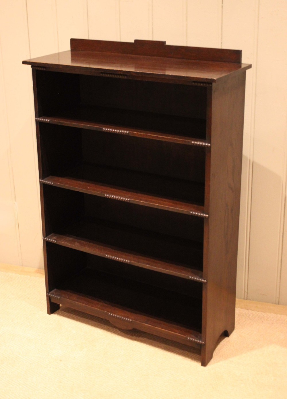 A dark oak open bookcase featuring four horizontal shelves with beaded front edges and a low raised gallery back. View X