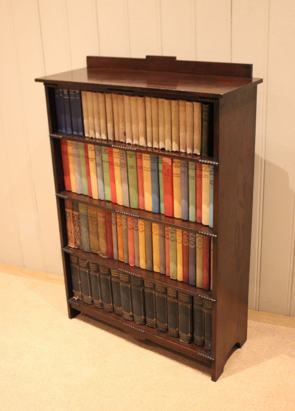 A dark oak open bookcase featuring four horizontal shelves with beaded front edges and a low raised gallery back. View XI