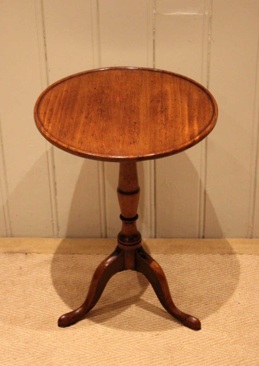 A circular mahogany tilt-top wine table with a turned central pedestal column and a tripod base featuring cabriole legs.