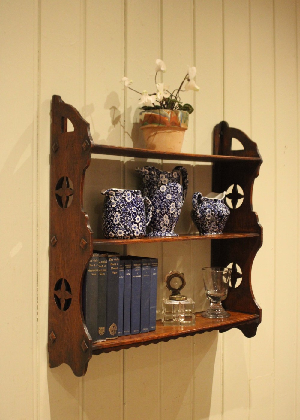 A late nineteenth-century dark oak wall-mounted shelf unit featuring three tiers and carved geometric cutouts along the side supports.