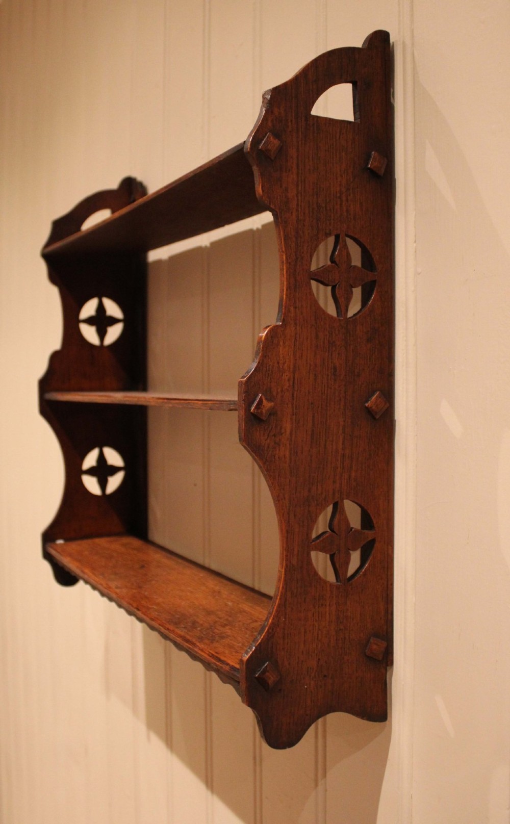 A late nineteenth-century dark oak wall-mounted shelf unit featuring three tiers and carved geometric cutouts along the side supports. View III