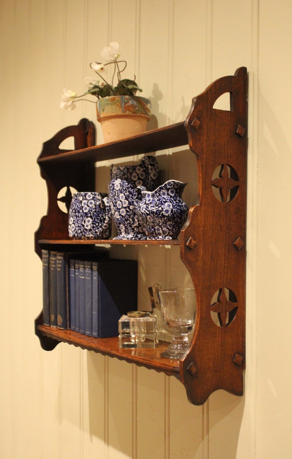 A late nineteenth-century dark oak wall-mounted shelf unit featuring three tiers and carved geometric cutouts along the side supports. View V