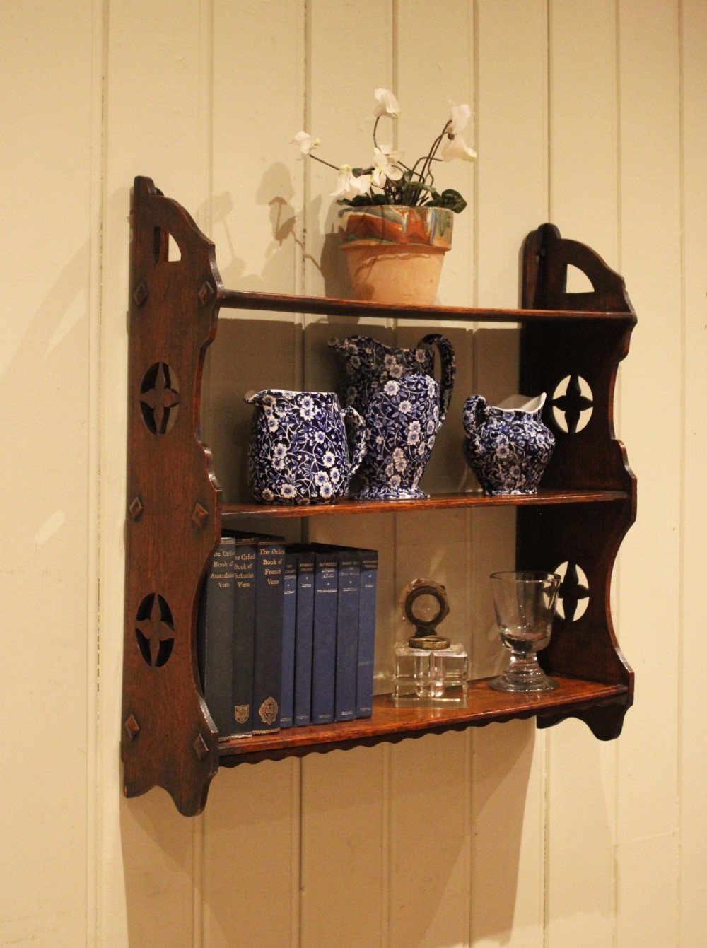 A late nineteenth-century dark oak wall-mounted shelf unit featuring three tiers and carved geometric cutouts along the side supports. View VI
