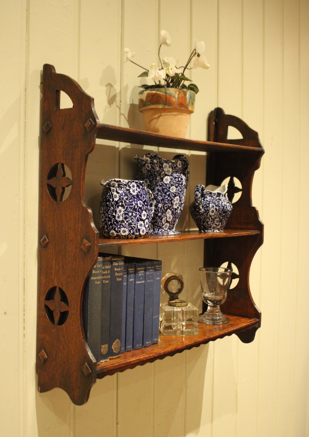 A late nineteenth-century dark oak wall-mounted shelf unit featuring three tiers and carved geometric cutouts along the side supports. View VII