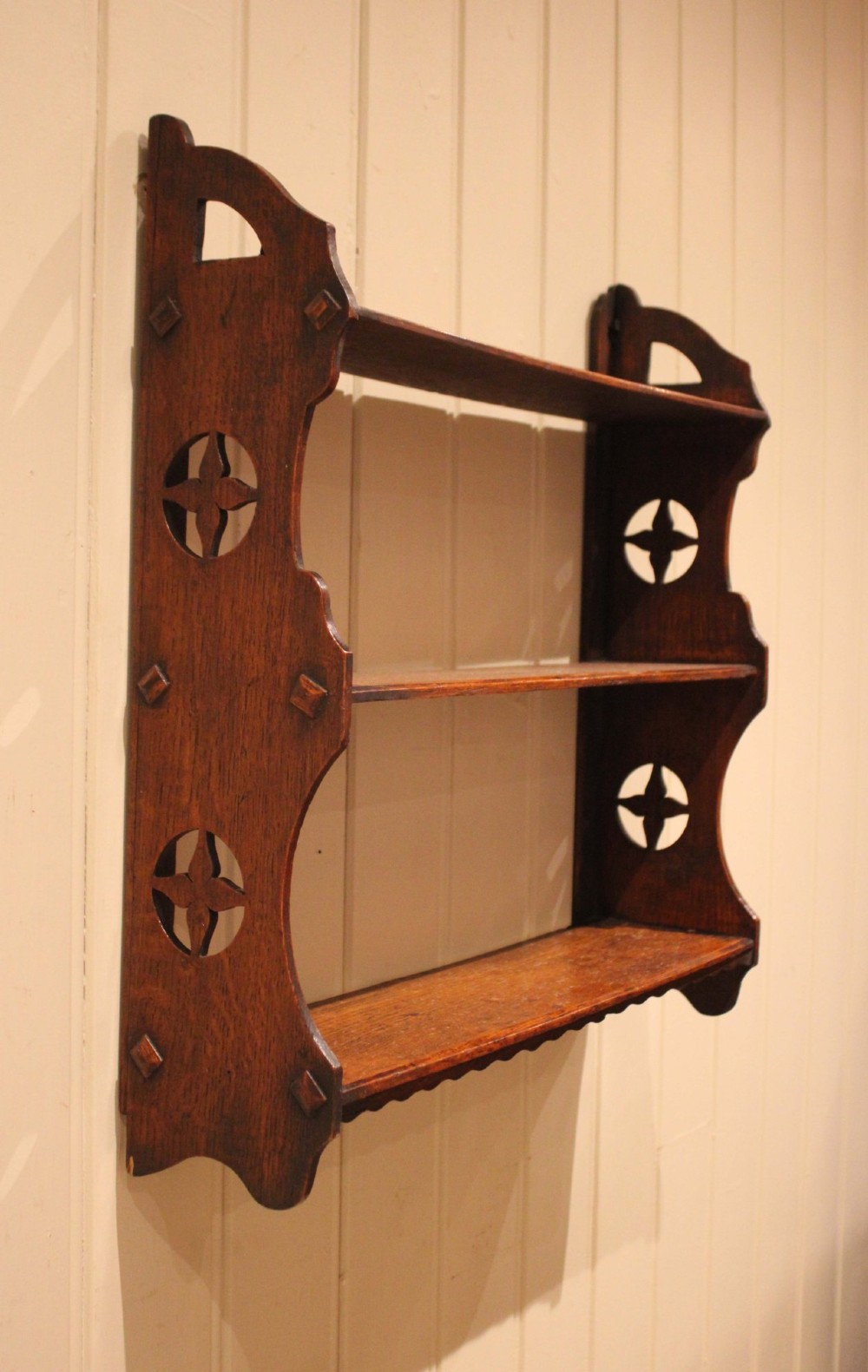 A late nineteenth-century dark oak wall-mounted shelf unit featuring three tiers and carved geometric cutouts along the side supports. View VIII