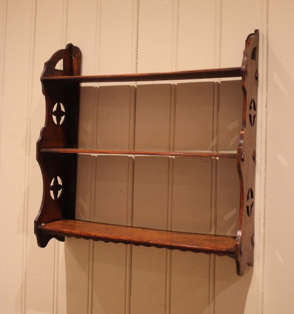 A late nineteenth-century dark oak wall-mounted shelf unit featuring three tiers and carved geometric cutouts along the side supports. View IX