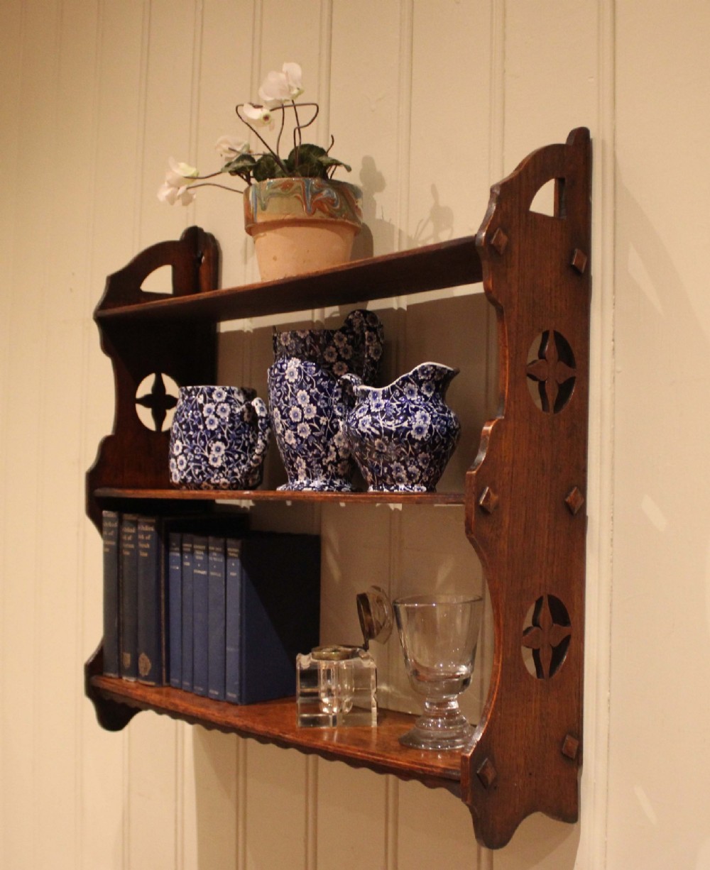 A late nineteenth-century dark oak wall-mounted shelf unit featuring three tiers and carved geometric cutouts along the side supports. View X